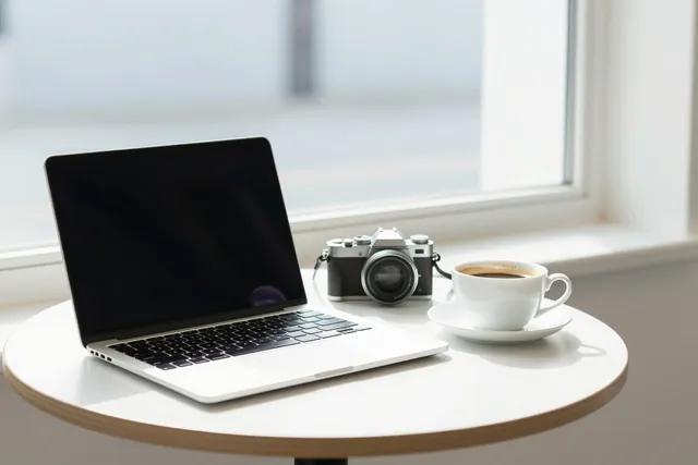 A sunlit café table with a laptop, a compact camera and a cup of coffee
